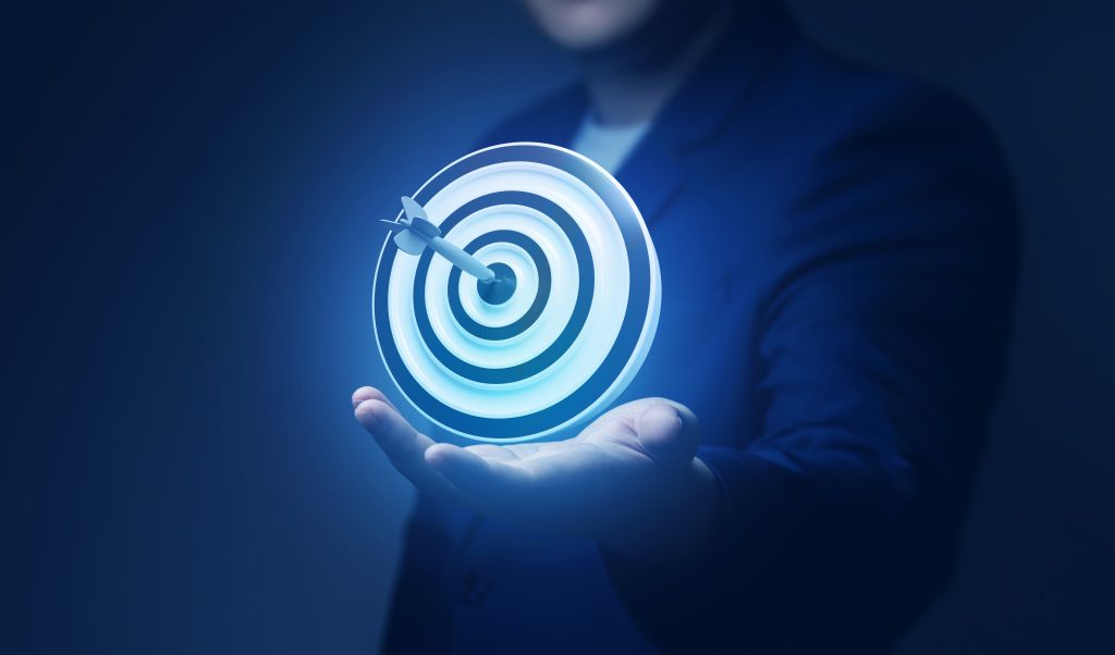 A hand holds a glowing target with an arrow striking the center, symbolizing focus and achievement.