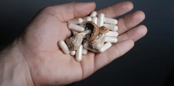 A hand holds a mix of dried mushrooms and white capsules against a dark background.