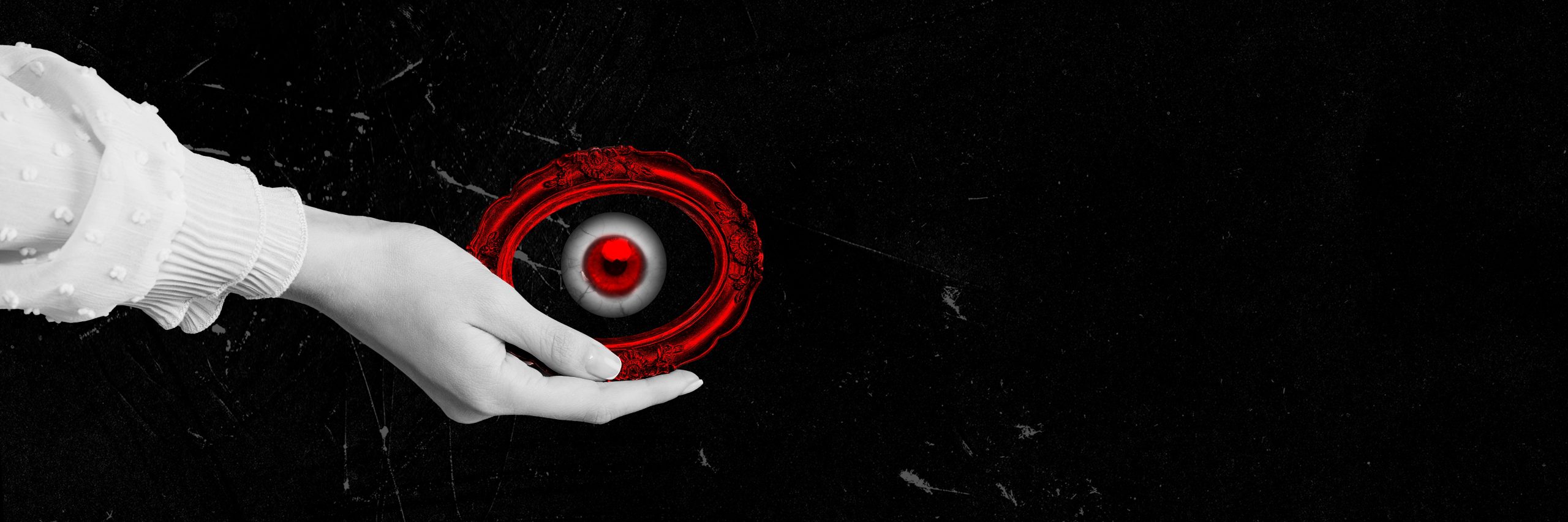 A hand holds a red, circular eye against a stark black background, creating a striking contrast.