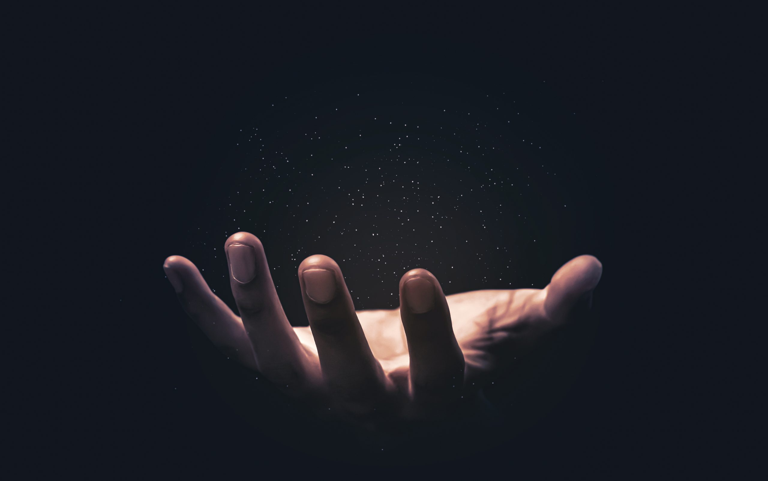 A hand reaches out, illuminated against a dark background, with sparkling particles floating above the palm.