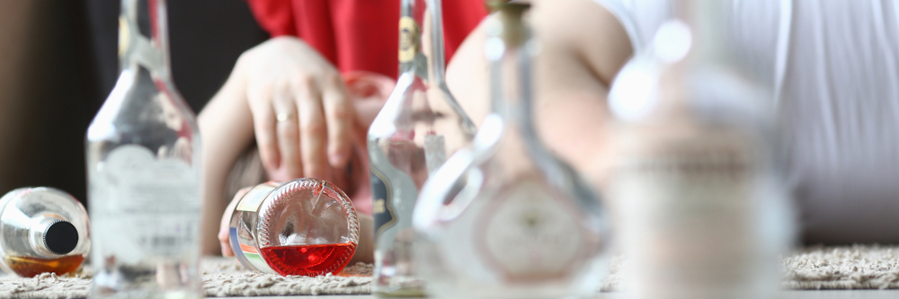 A hand reaches for a small bottle, surrounded by various empty glass containers on a textured surface.