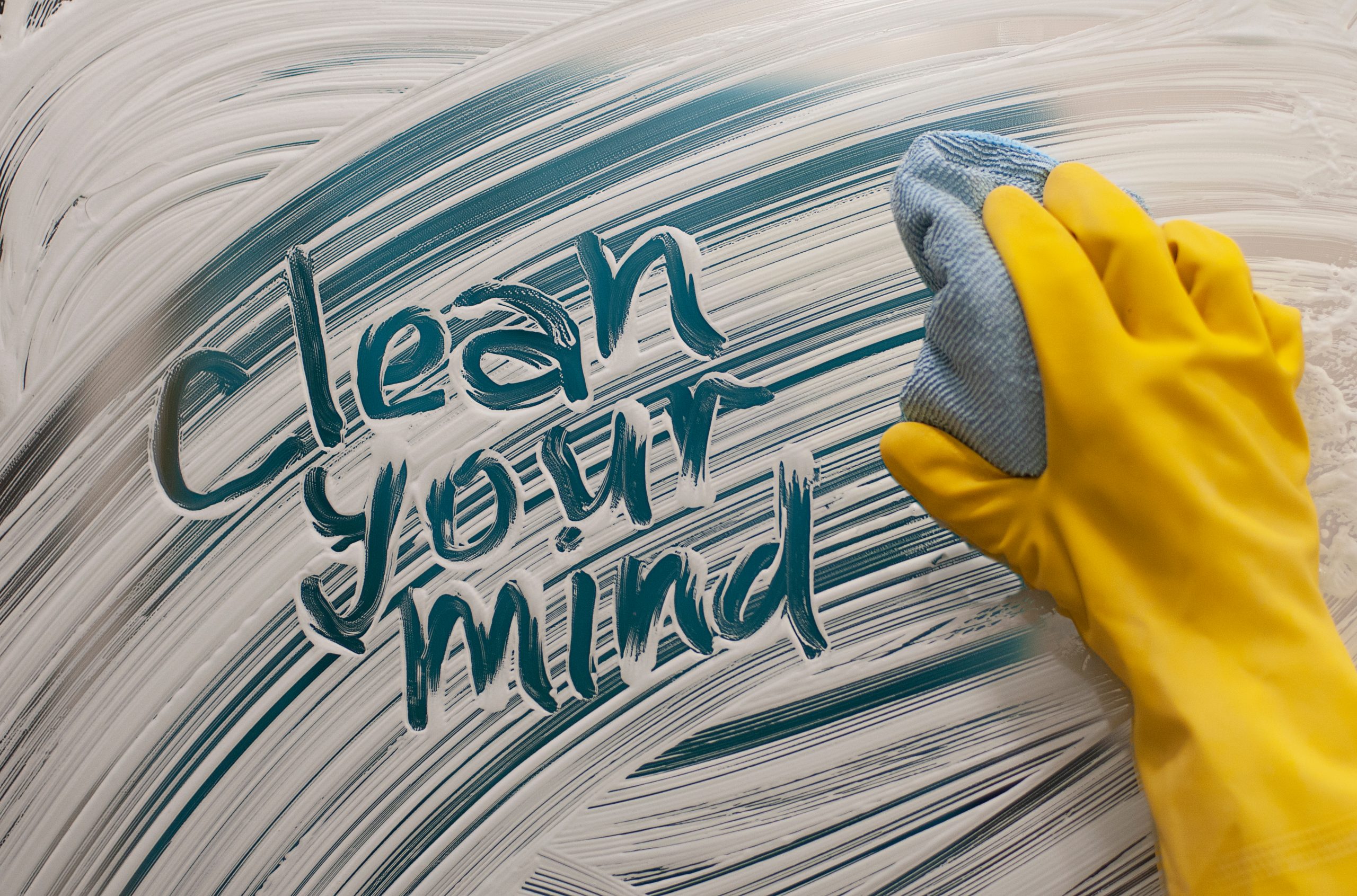 A hand in a yellow glove wipes a blue and white surface, revealing the phrase "clean your mind.