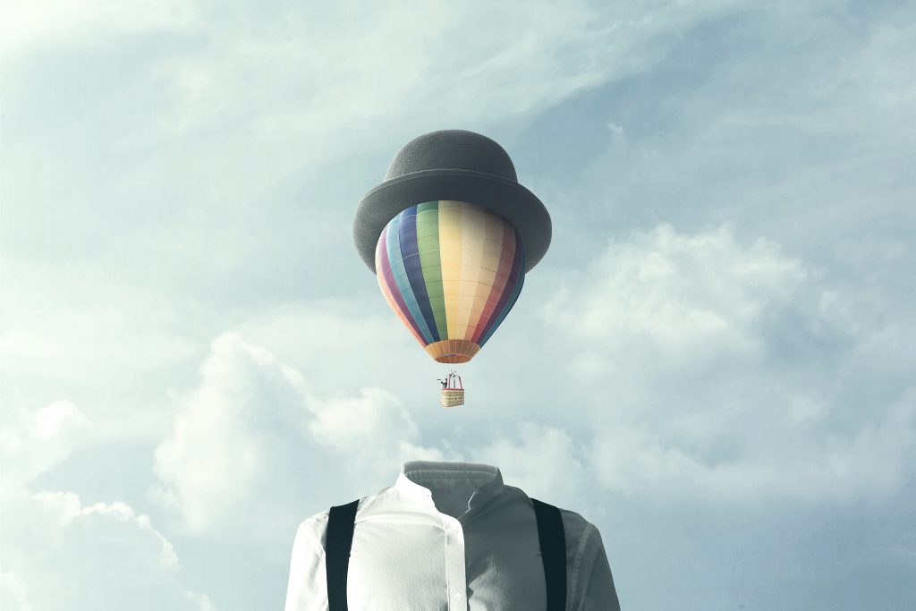 A headless figure in a bowler hat stands against a cloudy sky, with a colorful hot air balloon floating above.
