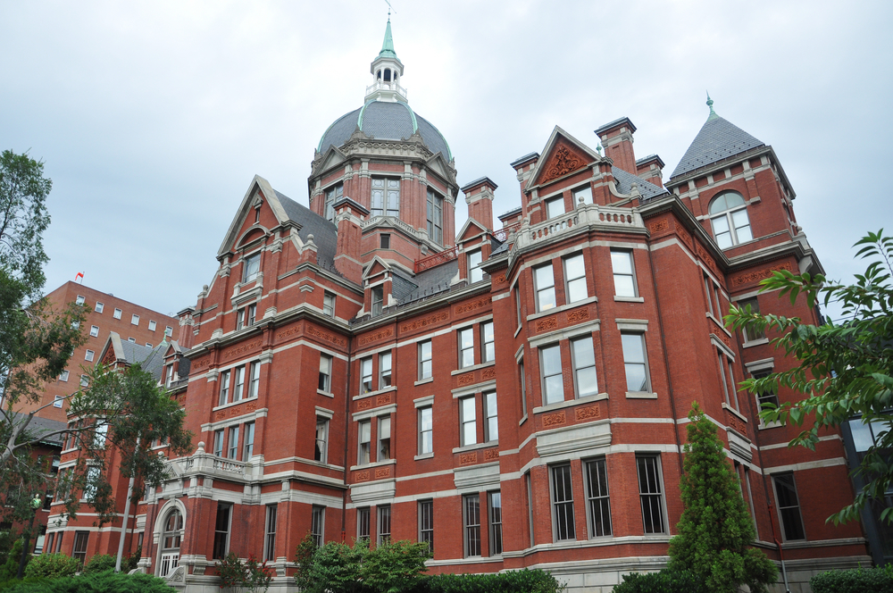 Historic red brick building with a large dome and intricate architectural details, surrounded by greenery.
