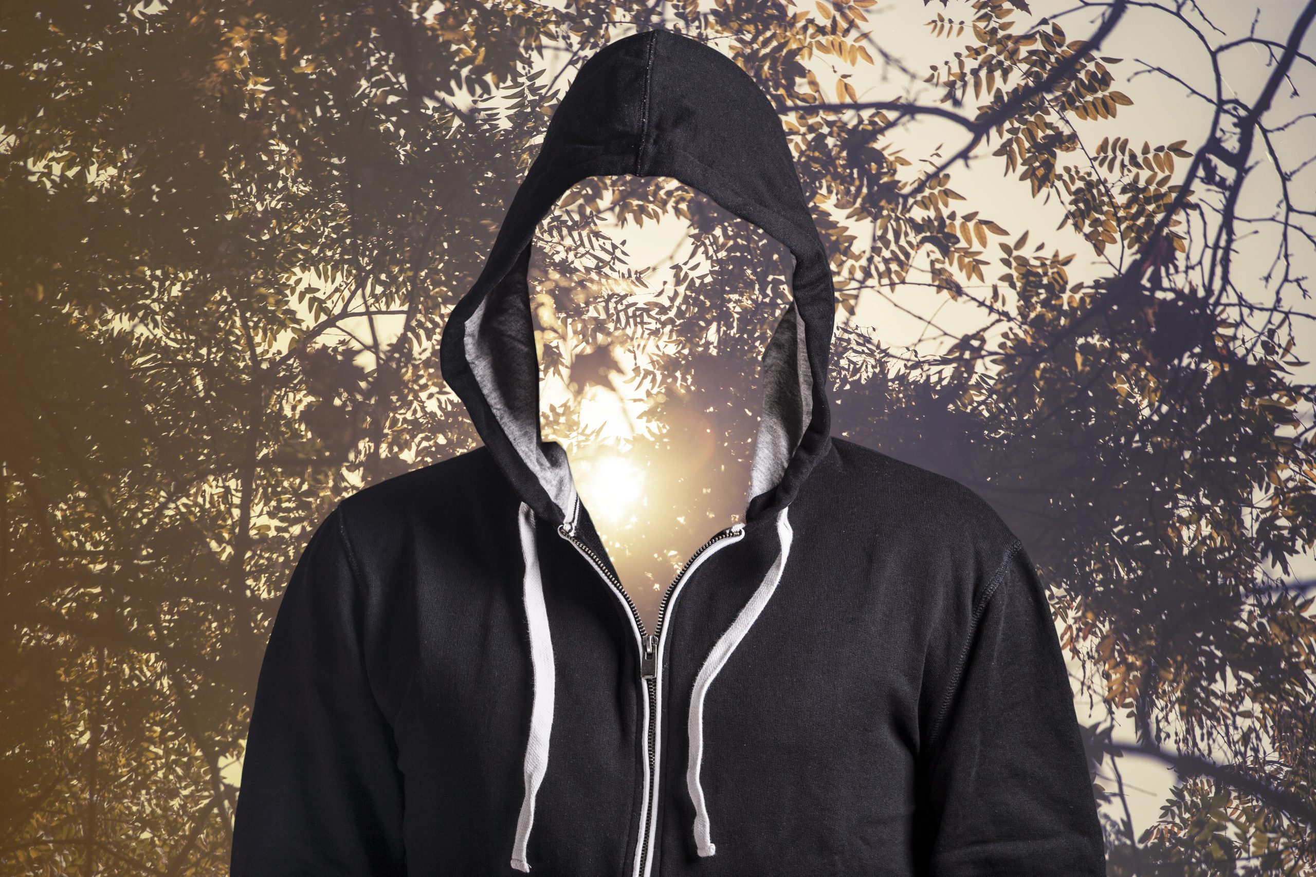 A hooded figure with a faceless silhouette stands against a backdrop of trees and sunlight.
