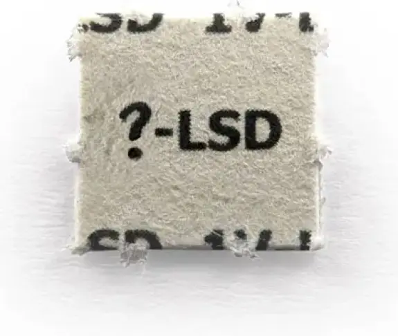 Square blotter paper with printed text "?-LSD" on a textured surface. Edges appear slightly frayed.