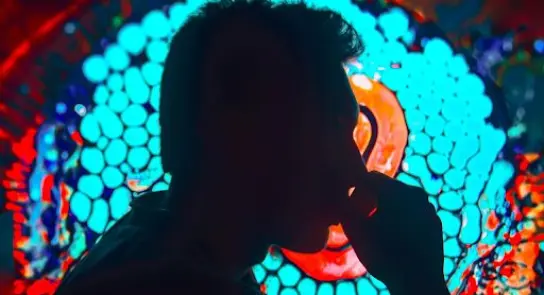 Silhouette of a person with hand to mouth, against a vibrant, abstract background of blue and red patterns.