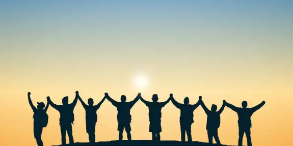 Silhouetted figures holding hands against a sunset, symbolizing unity and togetherness.
