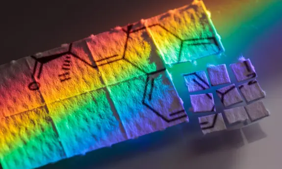 Colorful patterns of chemical structures on paper, illuminated by a spectrum of light, creating a vibrant rainbow effect.