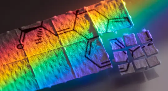 Colorful patterns of chemical structures on paper, illuminated by a spectrum of light, creating a vibrant rainbow effect.