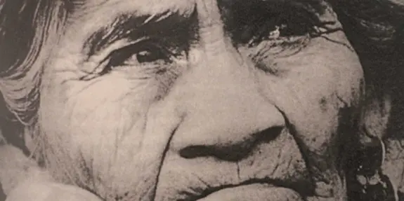 Elderly woman with deep wrinkles, intense gaze, and traditional earrings, conveying wisdom and resilience.