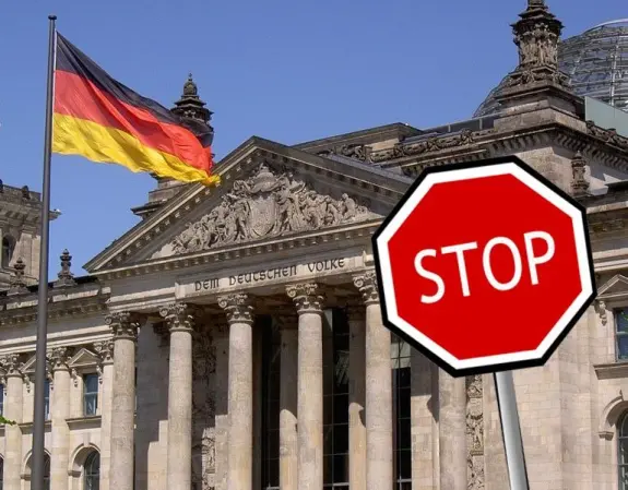 German flag waving in front of a historic building, with a prominent red stop sign in the foreground.