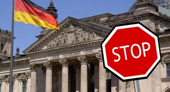 German flag waving in front of a historic building, with a prominent red stop sign in the foreground.
