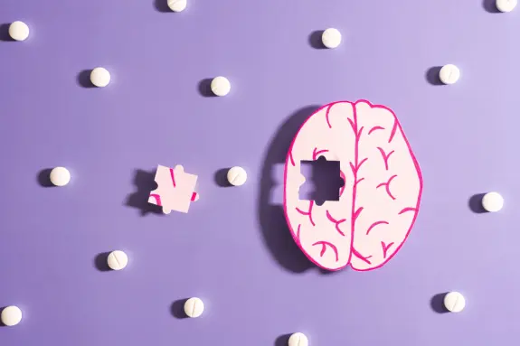 A pink brain puzzle piece missing a section, surrounded by white pills on a purple background.