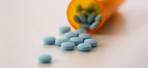 Scattered blue pills next to an overturned orange prescription bottle.