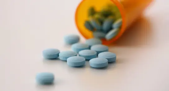 Scattered blue pills next to an overturned orange prescription bottle.