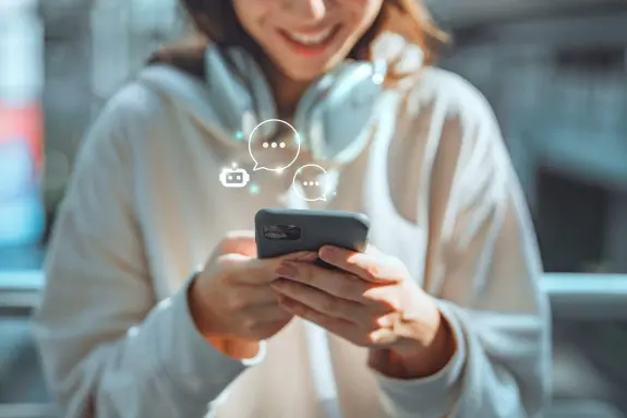 A young woman in a hoodie smiles while texting on her phone, wearing headphones, with chat bubbles above.