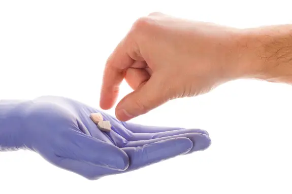 A gloved hand offers two pills to a reaching hand.