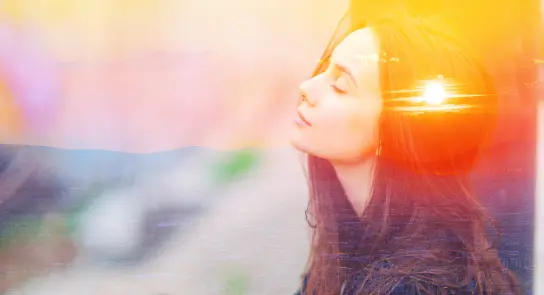A woman with long hair gazes peacefully upward, with a sunset blending into her silhouette.