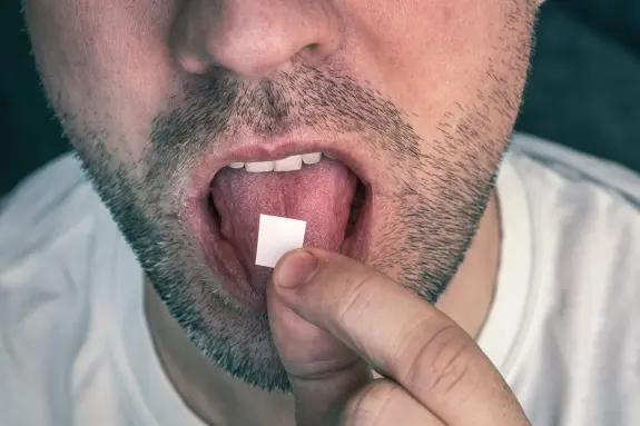 A man places a small square tablet on his tongue, preparing to dissolve it.
