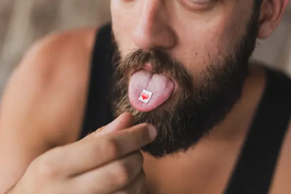 A man with a beard sticks out his tongue, revealing a small red heart-shaped sticker on it.