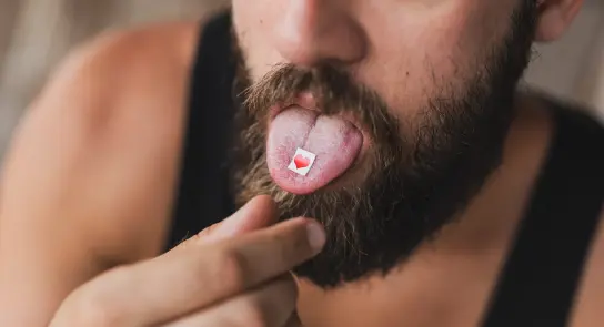 A man with a beard sticks out his tongue, revealing a small red heart-shaped sticker on it.