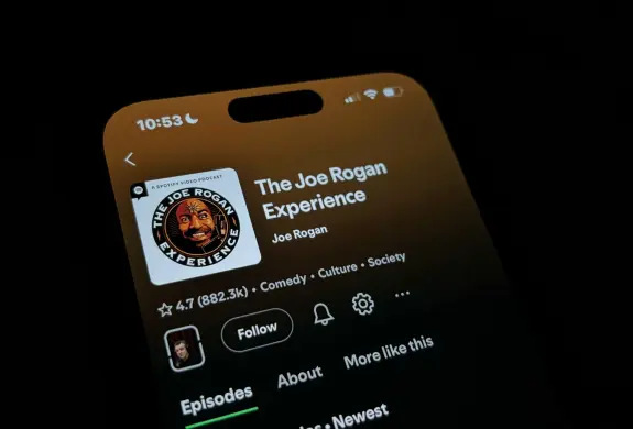Close-up of a smartphone screen displaying "The Joe Rogan Experience" podcast with ratings and episode options.
