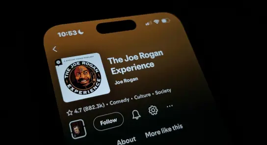 Close-up of a smartphone screen displaying "The Joe Rogan Experience" podcast with ratings and episode options.