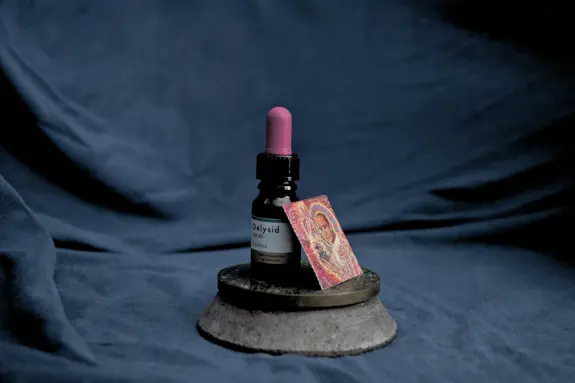 A dropper bottle with a pink cap beside a colorful psychedelic art piece, set on a circular concrete base against a dark b...