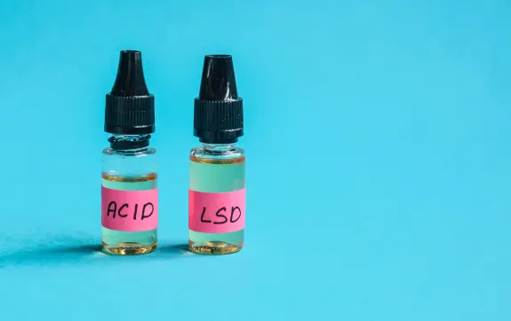 Two small glass bottles with black droppers, labeled "ACID" and "LSD," against a bright blue background.