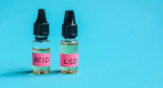 Two small glass bottles with black droppers, labeled "ACID" and "LSD," against a bright blue background.
