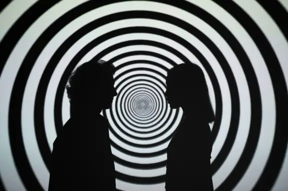 Silhouettes of two people facing each other against a swirling black and white spiral background.