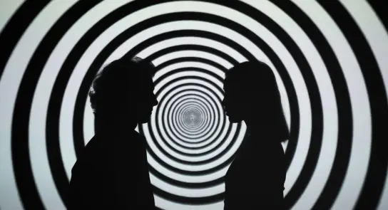 Silhouettes of two people facing each other against a swirling black and white spiral background.