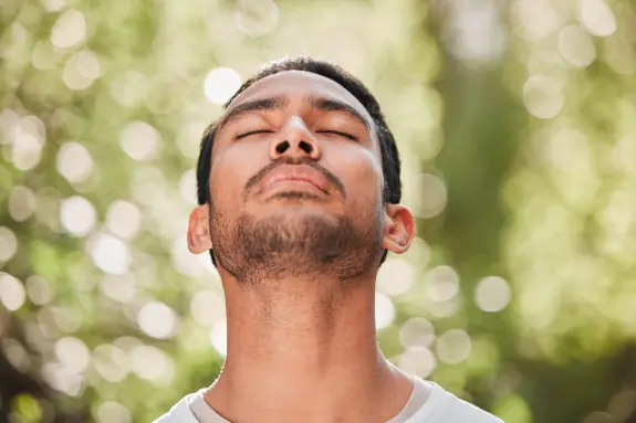 Man with closed eyes and a serene expression, surrounded by a soft, blurred green background.