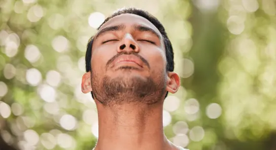 Man with closed eyes and a serene expression, surrounded by a soft, blurred green background.