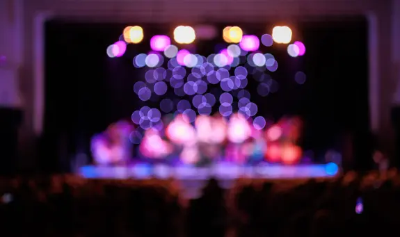 Blurry stage with colorful lights and silhouettes of musicians performing in the background.