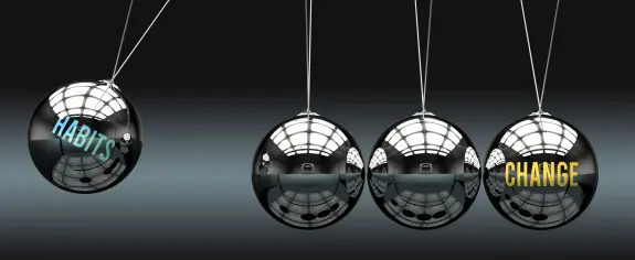 Three metallic spheres suspended by strings, with "HABITS" on the left and "CHANGE" on the right, reflecting light.