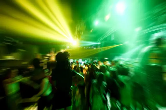 A vibrant dance floor filled with blurred figures, illuminated by green and yellow lights.