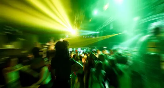 A vibrant dance floor filled with blurred figures, illuminated by green and yellow lights.