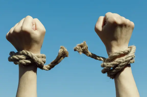 Two hands breaking free from ropes against a clear blue sky, symbolizing liberation and freedom.