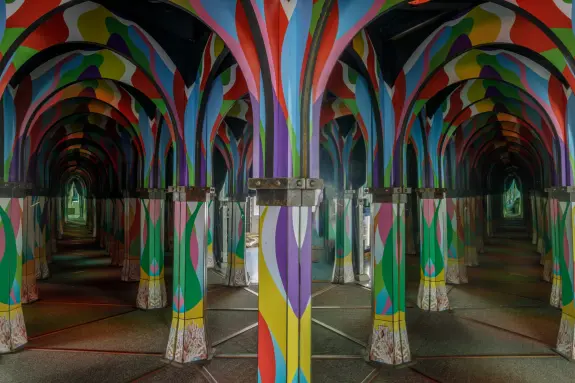 Colorful, patterned pillars create a vibrant, mirrored corridor, enhancing the sense of depth and reflection.