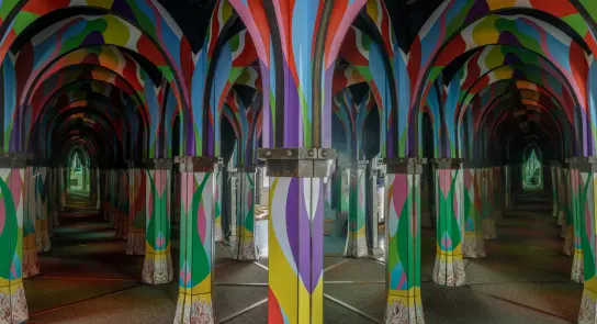 Colorful, patterned pillars create a vibrant, mirrored corridor, enhancing the sense of depth and reflection.