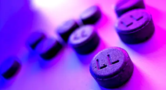 Black tablets with "LL" imprint scattered on a surface, illuminated by purple and blue lighting.