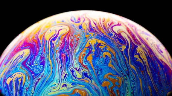 A colorful soap bubble with swirling patterns of blue, purple, and orange against a black background.