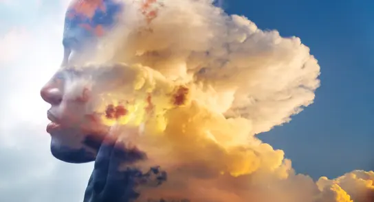 Silhouette of a woman's profile blended with vibrant clouds and a sunset sky, creating a dreamlike effect.