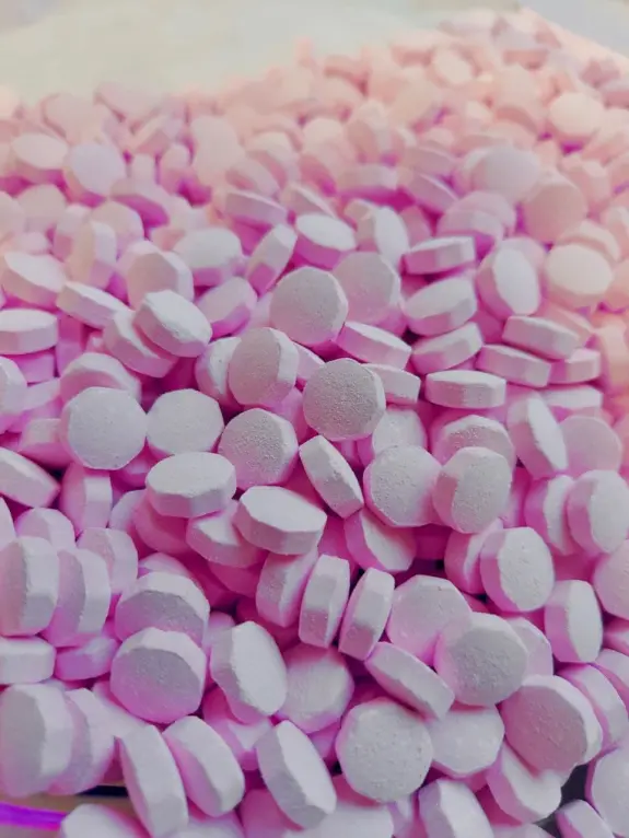 Scattered pink tablets with a round, flat shape, creating a textured surface against a light background.