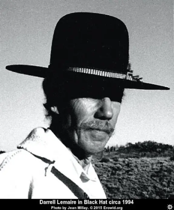 Black-and-white portrait of a man with a mustache wearing a wide-brimmed black hat, set against a desert landscape.