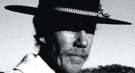 Black-and-white portrait of a man with a mustache wearing a wide-brimmed black hat, set against a desert landscape.