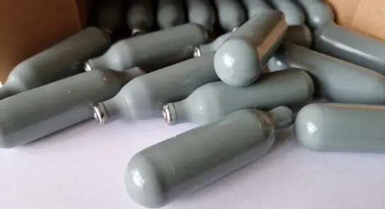 Gray gas canisters scattered on a white surface, some partially hidden behind a cardboard box.