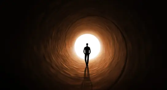 Silhouette of a person walking toward a bright light at the end of a dark tunnel.
